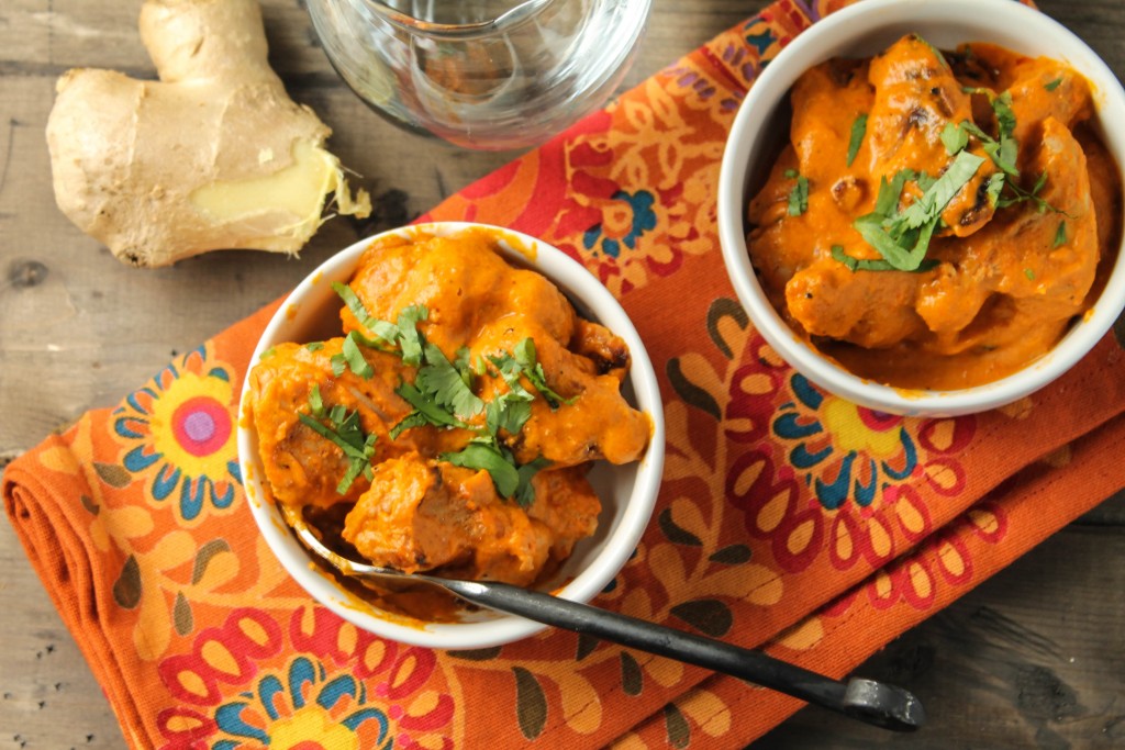 birds eye view of two small white bowls filled with tender chunks of chicken slathered in a tomato cream sauce on a deep orange paisley cloth