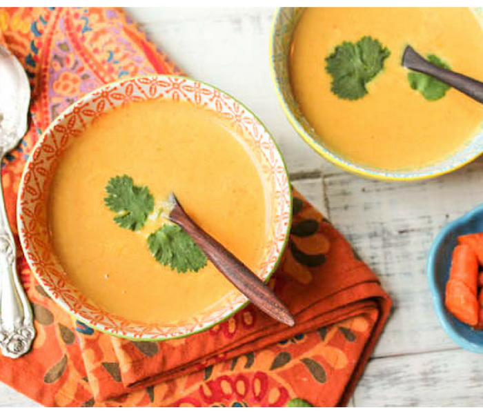 two bowls of orange carrot soup on an orange paisley cloth from overhead