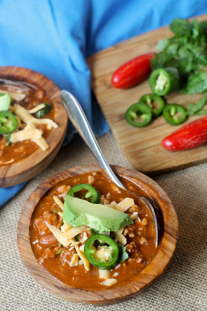 two olive wood bowls filled with chili topped avocado, cilantro, and fresh jalapeños