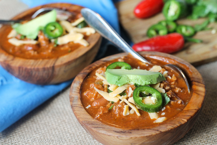 two bowls filled with picto pean and ground beef stew with chili, avocado, cheese on rustic surface