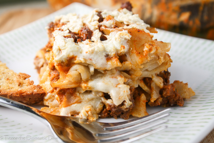 a square of noodle casserole layered with a creamy white cheese sauce and red meat sauce atop a white plate