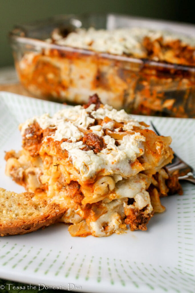 a cut square of homemade lasagna on a white plate with a full pan in background