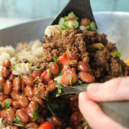 two hand help wooden spoons tossing the ingredeints for a tex-mex pasta lad in a silver bowl