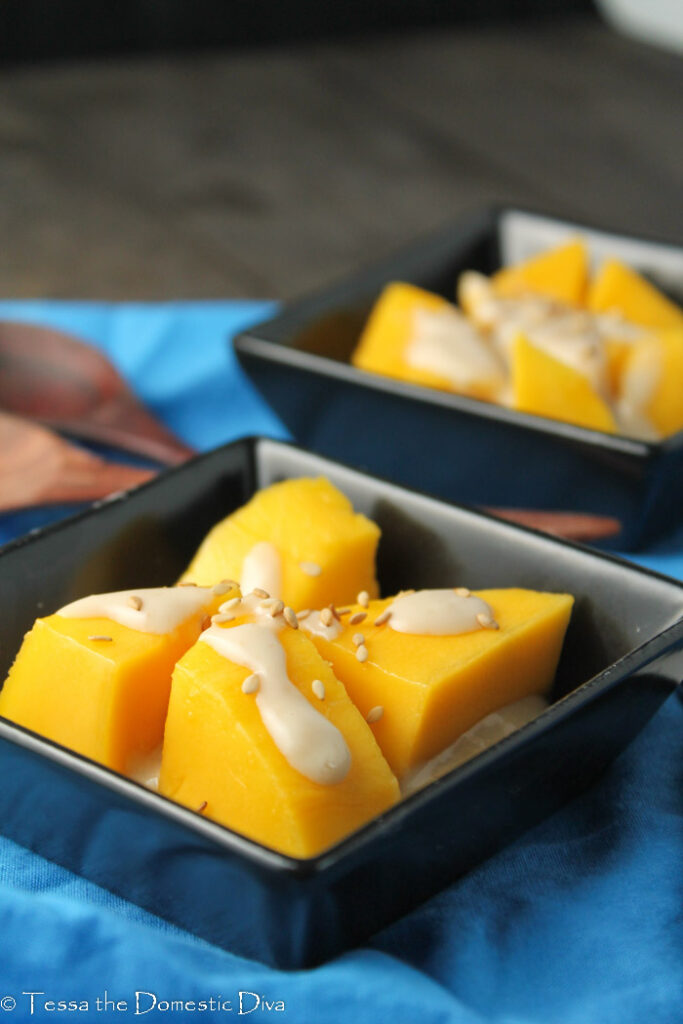 yellow orange paleo thai mango dessert with a sweet salty coconut sauce in square black dishes on a bright blue cloth