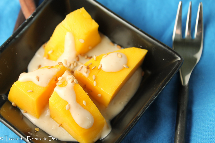 overhead shot of four chunks of peeled Thai mango drizzled in a coconut sauce and sprinkled with sesame seeds
