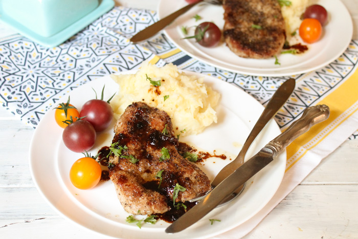 horizontal image of a simple pork tenderloin recipe with a parsley garnish plated on a white plate with some mashed potato and fresh cherry tomatoes