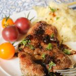 pork medallion seared in a skillet with a savory drizzleon a white plate with a mashed cauliflower and an heirloom cherry tomato side.