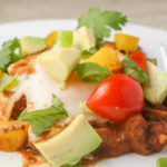 a white plate filled with a molten poached aegg atop a bed of refried beans with fresh cherry tomatoes and chopped cilantro