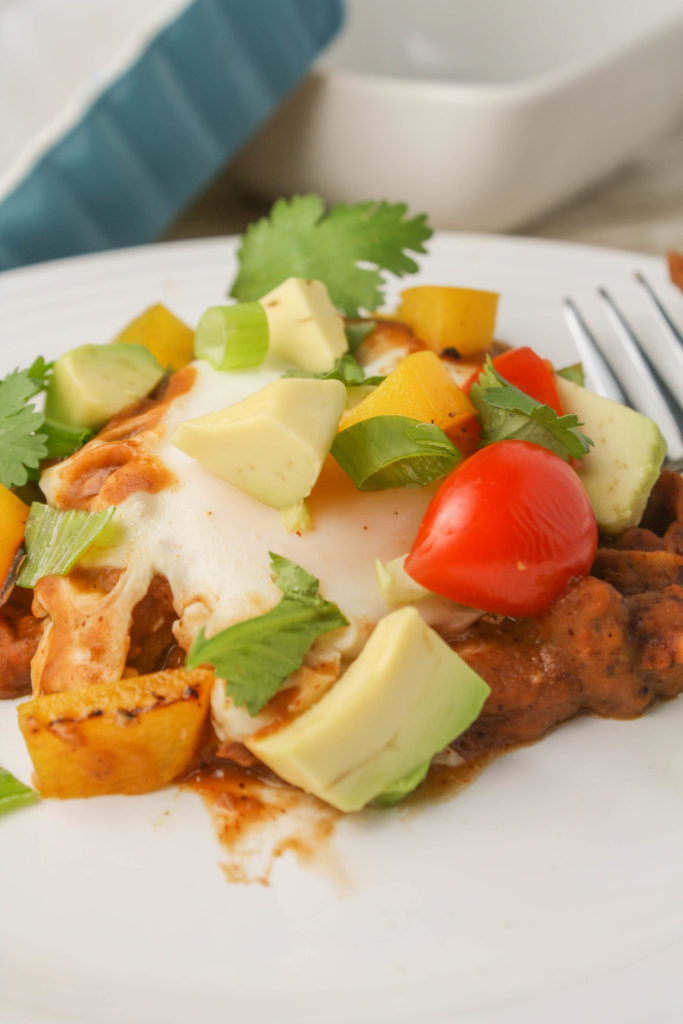 a gently poached egg on top of a bed of Mexican refried beans with a garnish of chopped avocado, cherry tomato, and cilantro