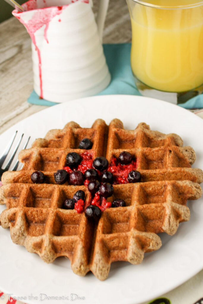 a golden waffle atop a white plate with fresh berries on top