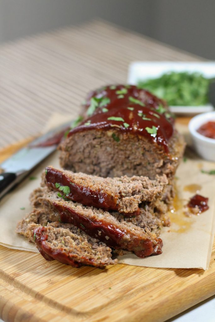 sliced meatloaf from the front with a glistening tomato sauce topping and a sprinkling of chopped parsley.