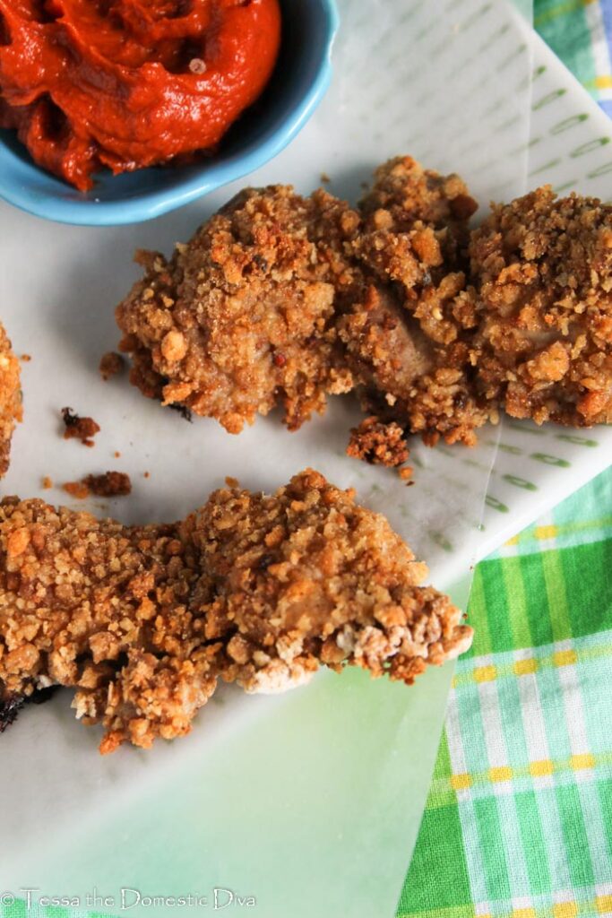 two chicken tenders coted in a crispy coating atop a white plate with homemade ketchup