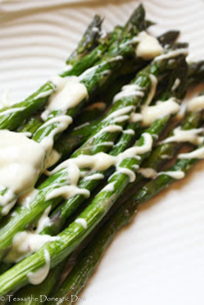 grilled asparagus spears drizzled in a white garlic lemon aioli on a white plate