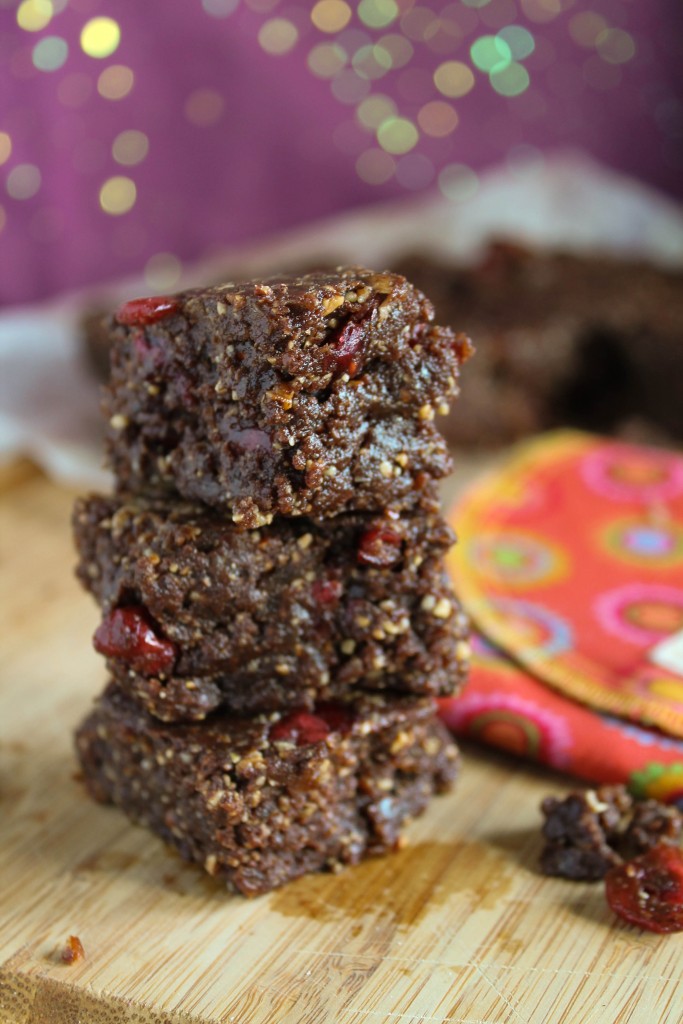 a stack of three nutty chocolate energy bars studded with cranberry bits on a wooden cutting board