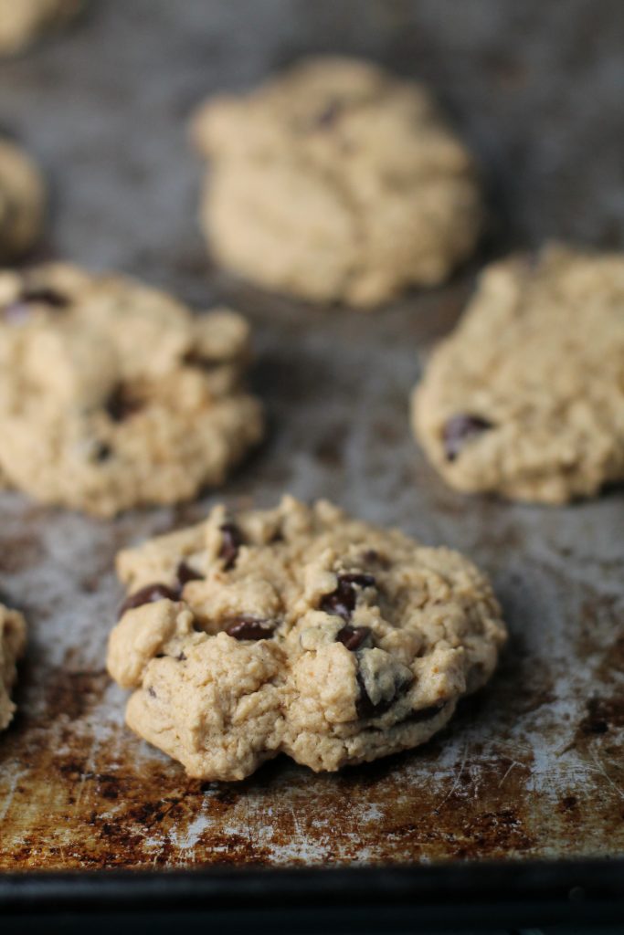 vertical image of a chocolate chip cookie on a well worn steel cookie sheet