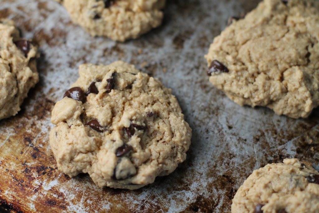 close up of a chocolate chip studded cookies on a worn steel cookie sheet