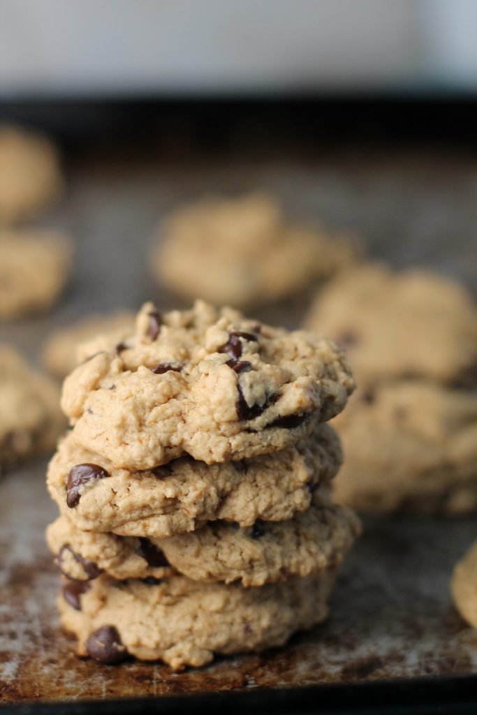 4 stacked chocolate studded cookies on a worn steel cookie sheet