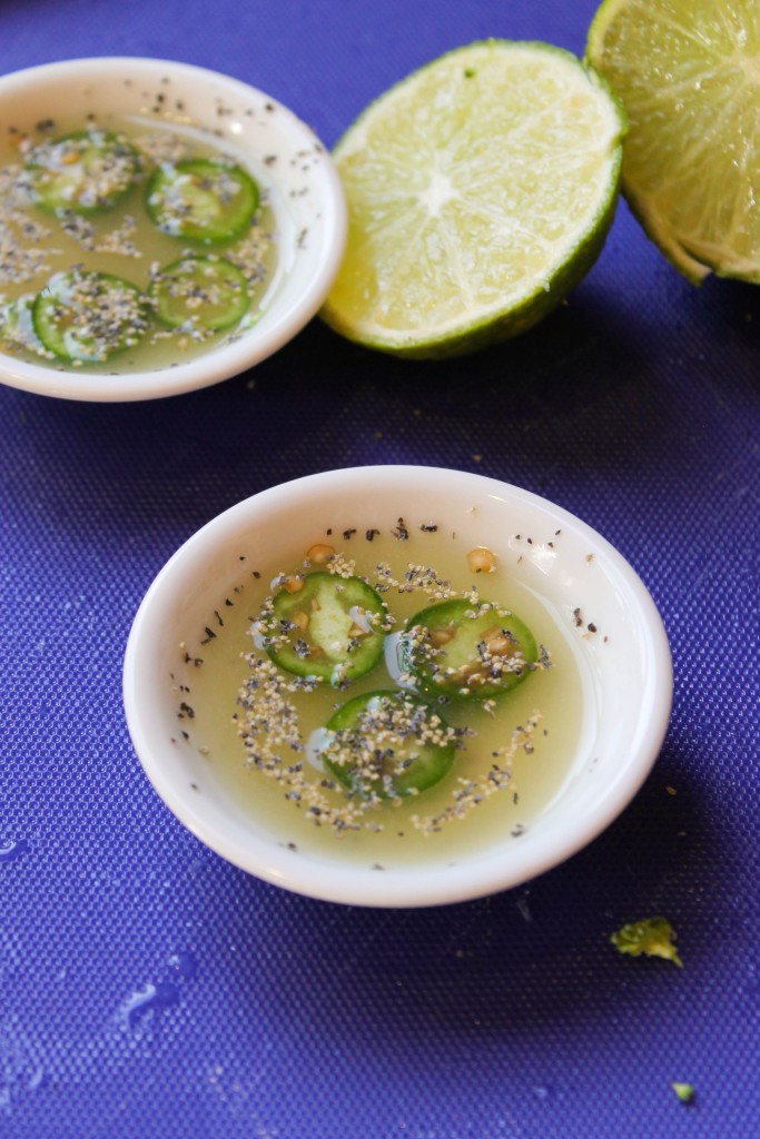 two white dipping dishes filled with lime juice, pepper, and sliced serrano peppers on a royal blue cutting board