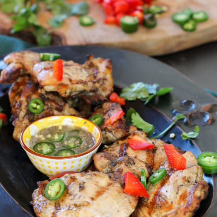 a black plate filled with boneless grilled chicken thighs with peppers, lime juice, and fish sauce.