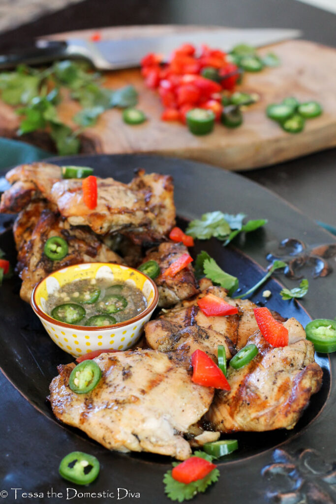 a black plate filled with boneless grilled chicken thighs with peppers, lime juice, and fish sauce.