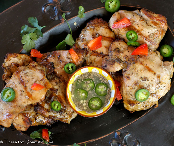 birds view of a black plate of grilled vietnamese chicken thighs with chili lime sauce.