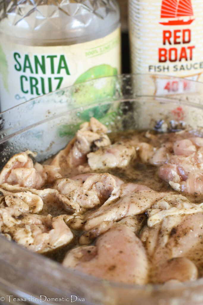 a bowl of boneless chicken thighs in a marinade of fish sauce and lime juice.