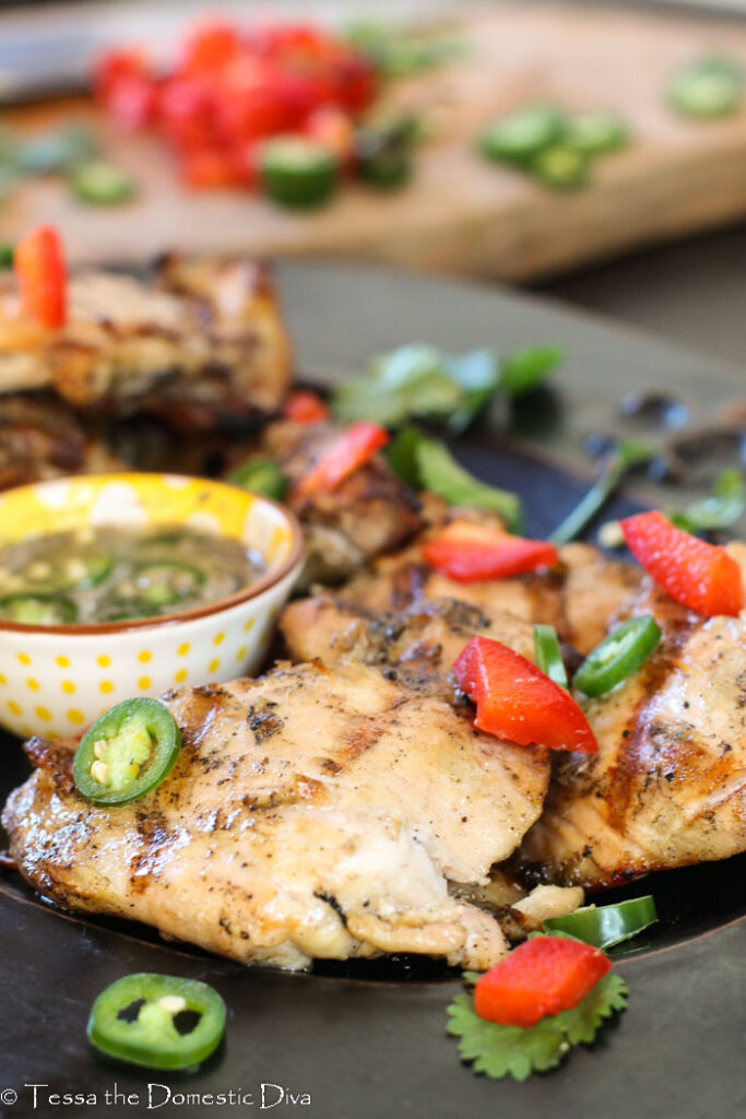 a boneless chicken thigh with grill lines served with sliced jalapenos and a fish sauce and lime accompaniment.