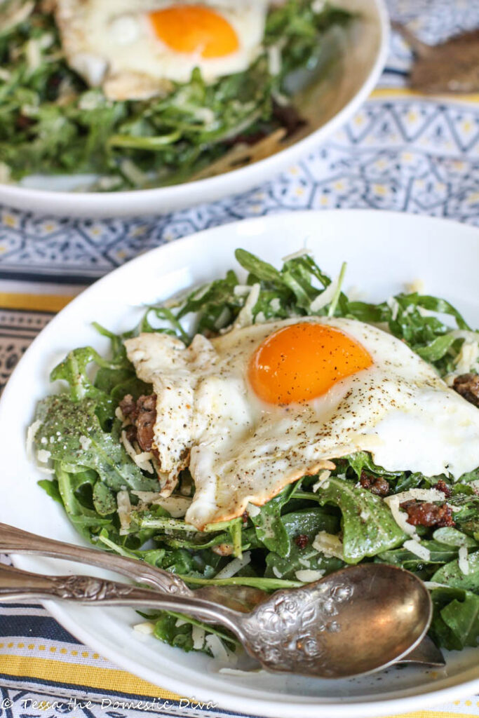 two white bowls filled with arugaa and shaprp dubliner cheese with a sunny side up egg and sausage