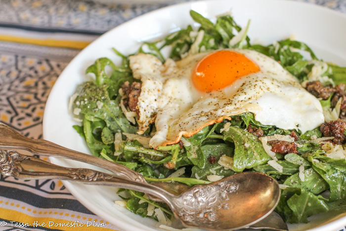 an egg with a molten yolk draped over a dressed salad with ground cooked sausage and white cheese shreds