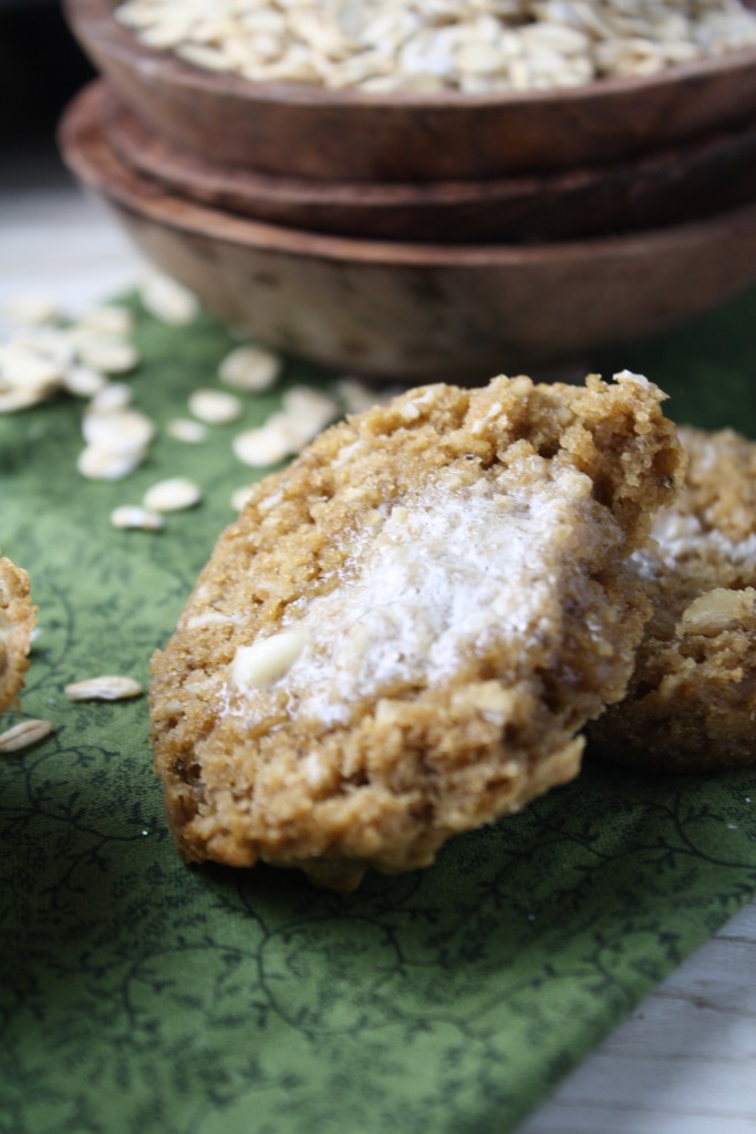 a halved oatmeal muffin slathered in melted butter on a green cloth with rolled oats in a dark wooden bowl in the background