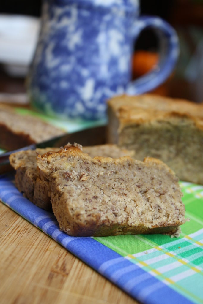 several slices of banana flecked bread atop a wooden cutting board and blue and lime cloth