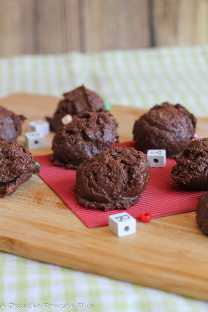 small round chocolate and oat cookie arranged on a wooden cutting board with playful letter beads and a red piece of cardboard