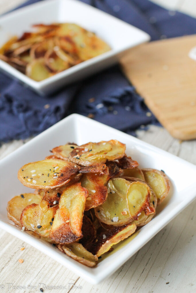 two white bowls filled with sliced roasted potatoes.