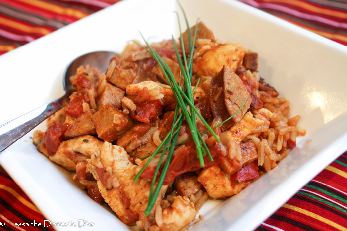 a sqaure white dish with a cajun tomato rice, chicekn, and sausage dish topped with fresh chives