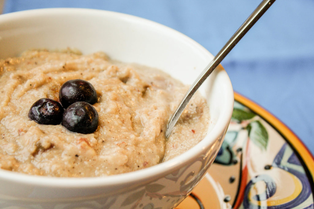 fron view of a white bowl filled with millet porridge and fresh berries with spoon and blue background