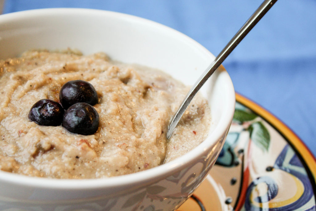 an eye level close up of a creamy gluten free porridge topped with three fresh blueberries in a white bowl on a Mexican pottery plate