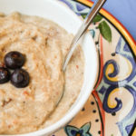 white bowl filled with cream millet porridge and topped with 3 fresh blueberries with a Mexican pottery plate