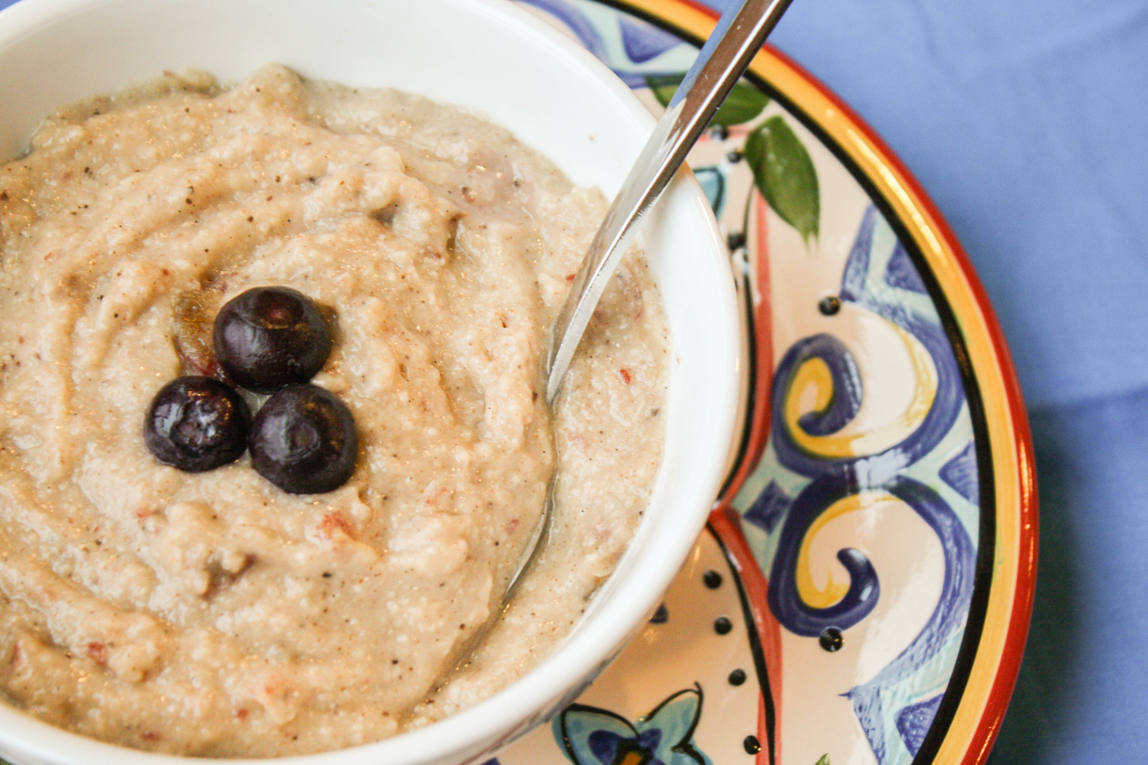 white bowl filled with cream millet porridge and topped with 3 fresh blueberries with a Mexican pottery plate