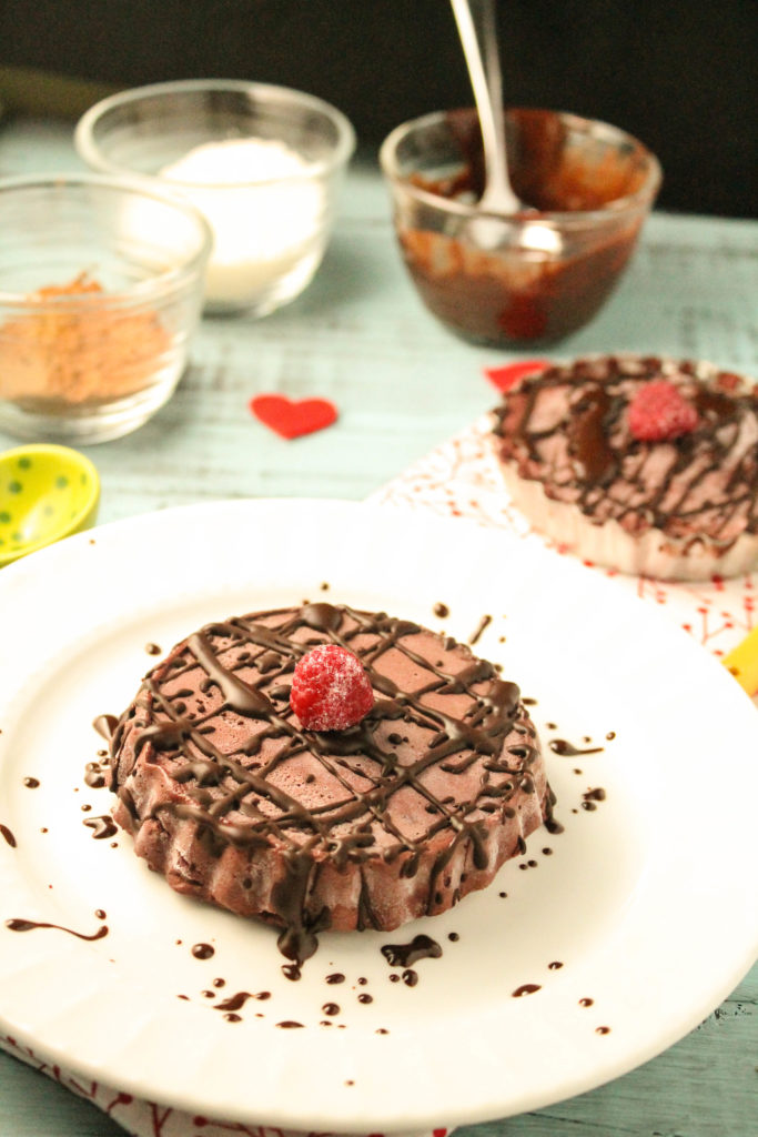 a small chocolate raspberry tart on a white plate with chocolate drizzle