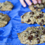 chococlate chip cookies arranged on a blue cloth with a child's hand reaching for a cookie