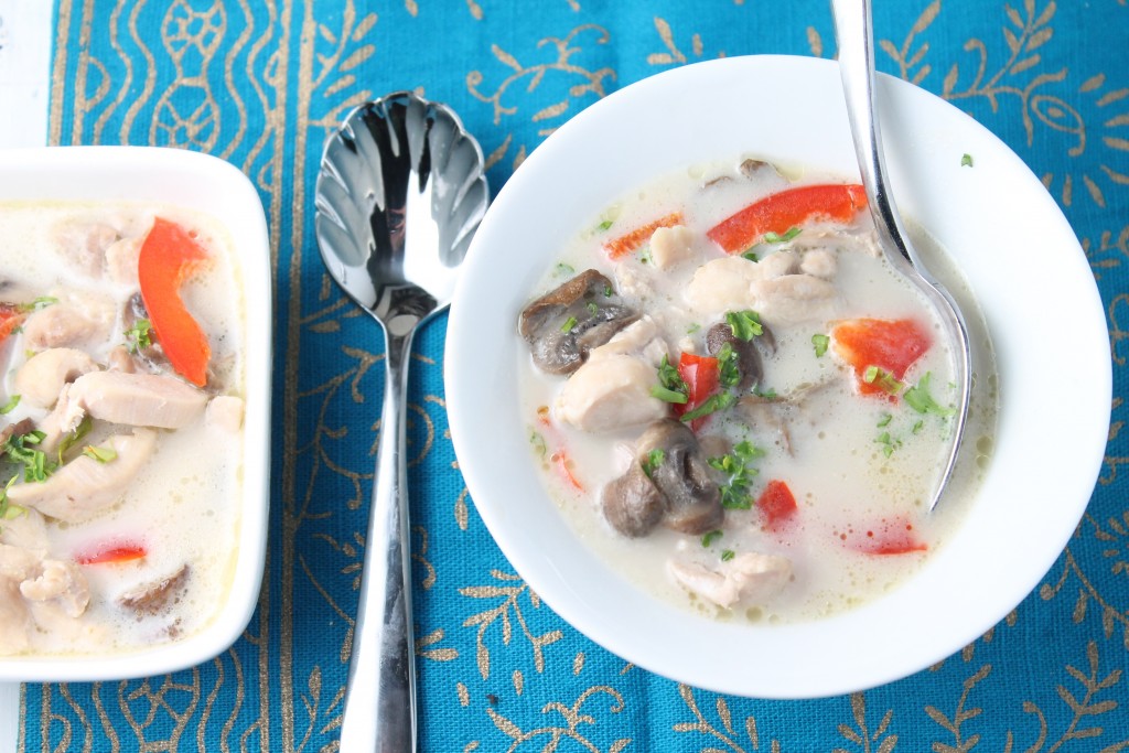 pinterest ready birds eye view of creamy white coconut milk soup with mushroom, chicken pieces, red peppers, and cilantro in white bowls on a thai patterned turquoise linen