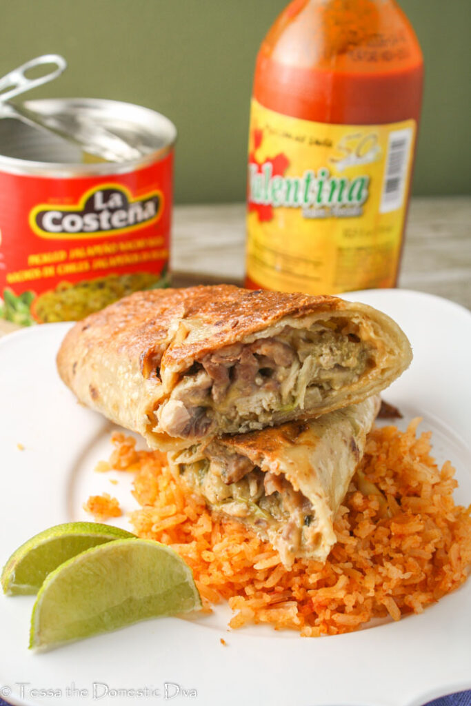 a sliced crispy chicken burrito atop a bed of Mexican red rice on a white plate with a lime wedge