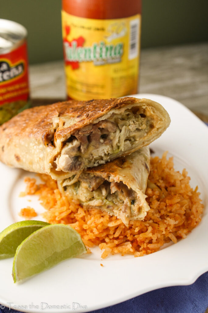 baked chimichangas halves stacked ona white plate with red rice and a lime wedge