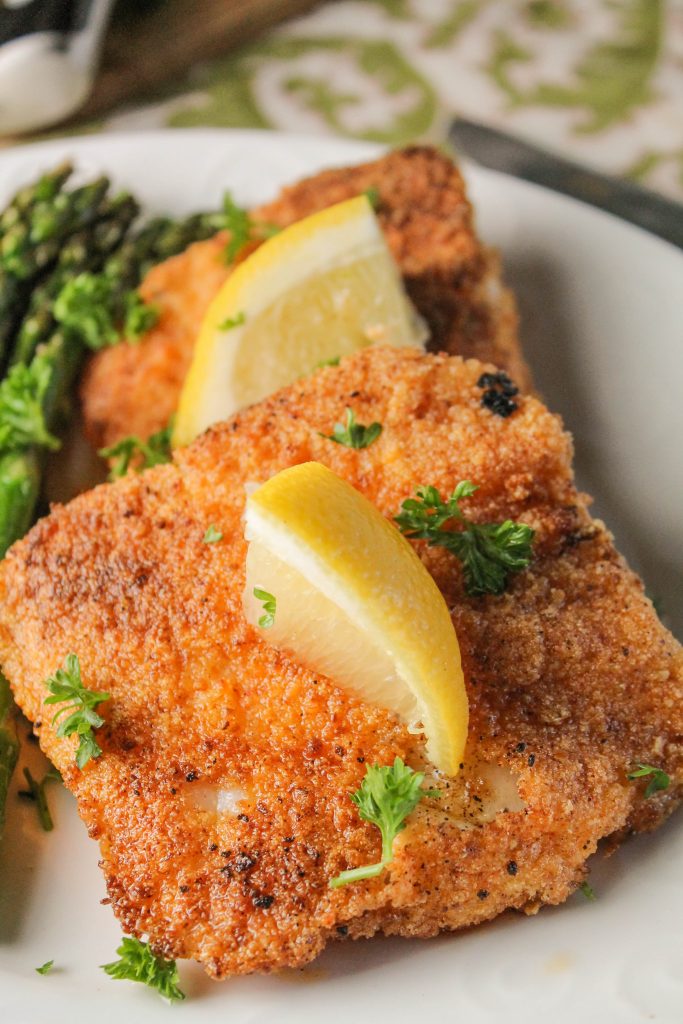 golden pan fried breaded fish fillets sprinkled with chopped parsley and a lemon wedge