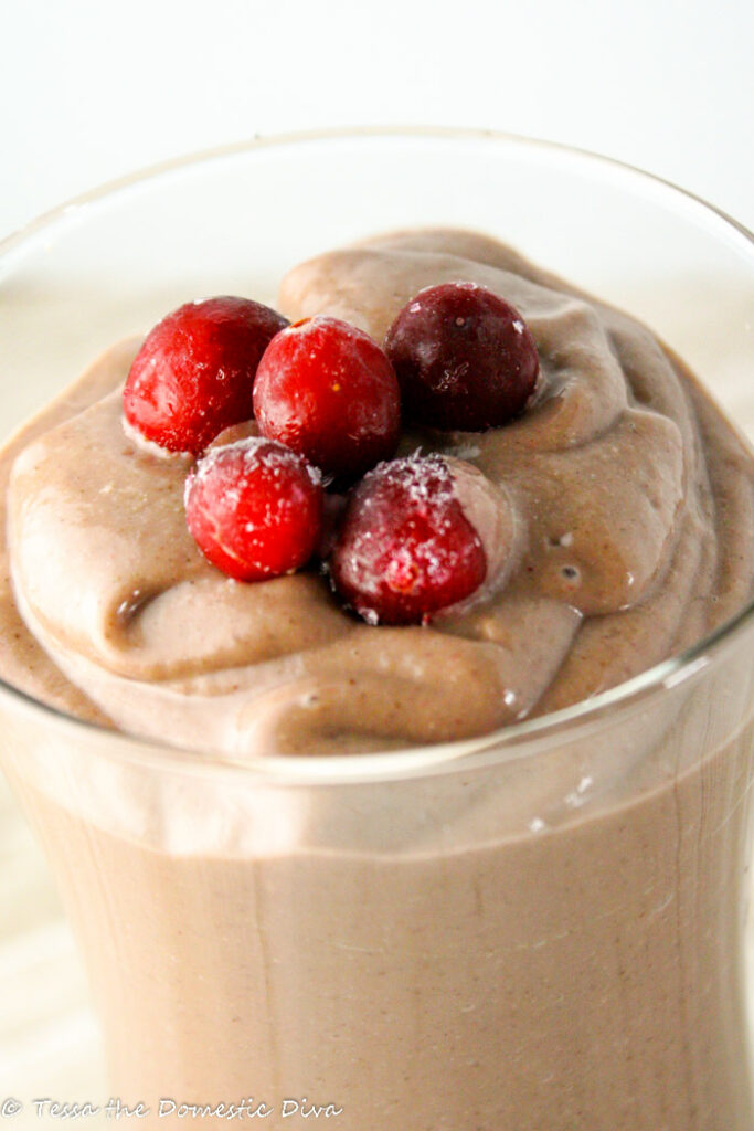 a clear glass of a creamy berry smoothie topped with frozen red berries