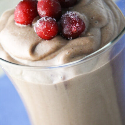 a clear glass filled with a creamy and thick berry smoothie topped with frozen berries