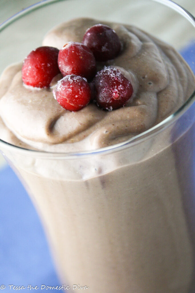 a clear glass filled with a creamy and thick berry smoothie topped with frozen berries
