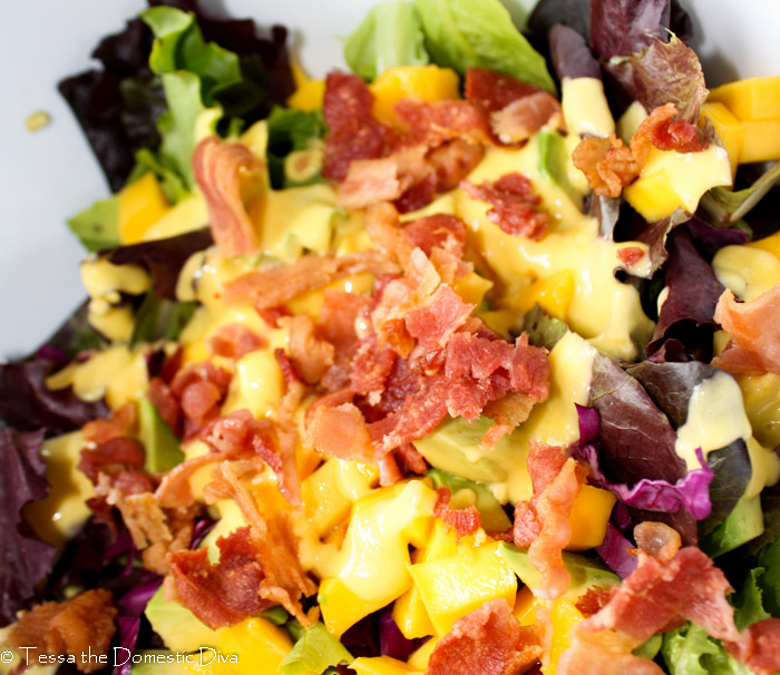 vibrant yellow mango vinaigrette drizzled on a mixed greens and bacon salad