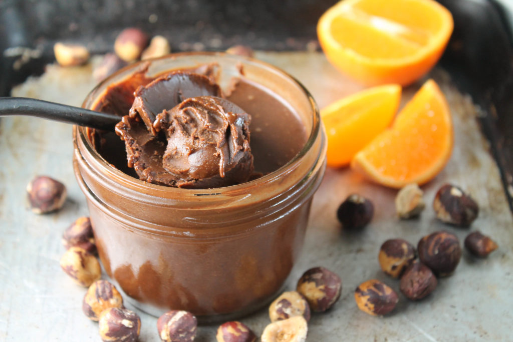 nutella in a mason jar with a spoon scooping some up, orange slices in background