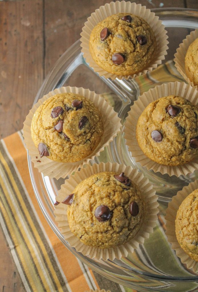 pumpkin chocolate chip muffins in unbleached paper liners arranged on a clear cake late atop a fall color striped linen